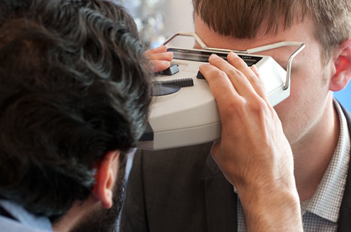 Optician checking boy's eyes with device
