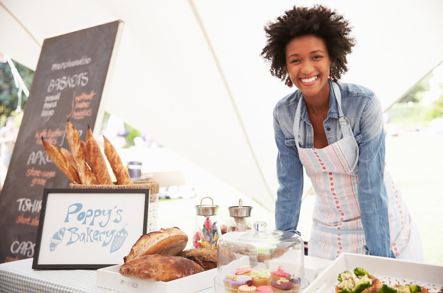 Female bakery employee smiling, leaning on counter with baked goods